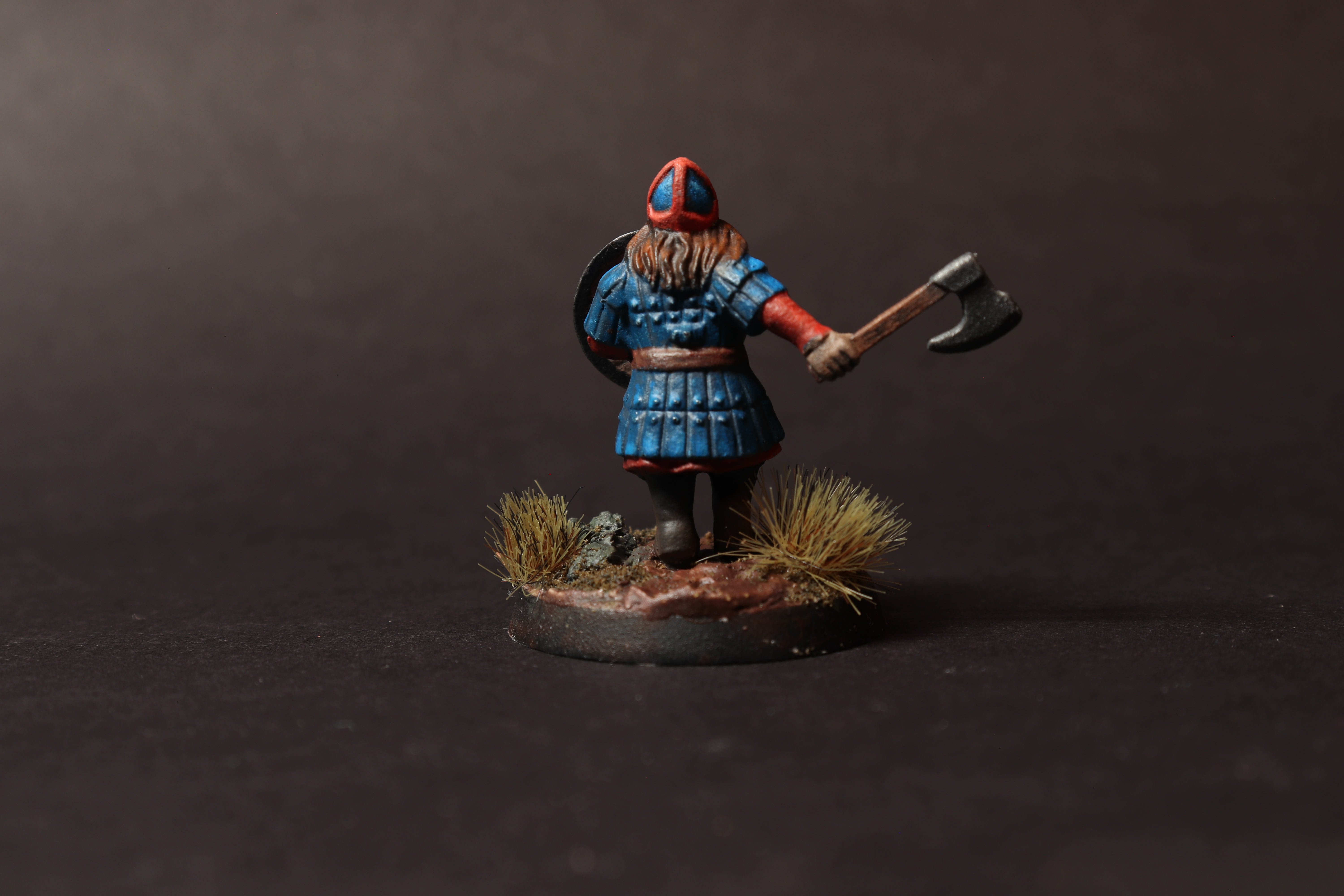 Back view of the dwarf warrior miniature showing blue armor plates, red sleeves, hair, axe, and tufts on the base.