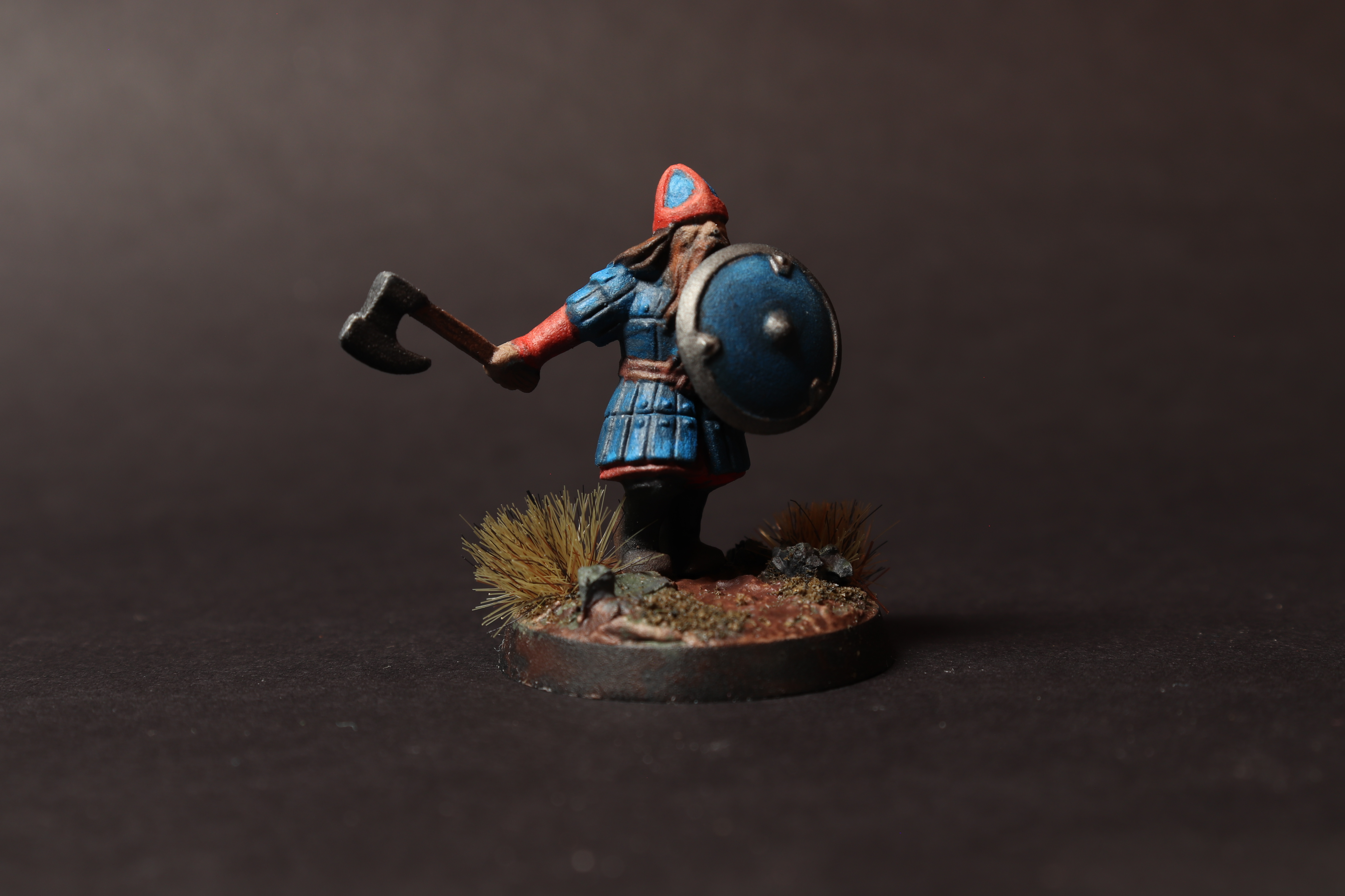 Right angle view of the dwarf warrior miniature with blue armor, axe, shield, and basing details.